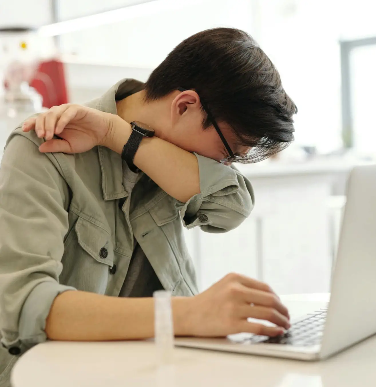 Homme toussant dans son bras devant son ordinateur portable
