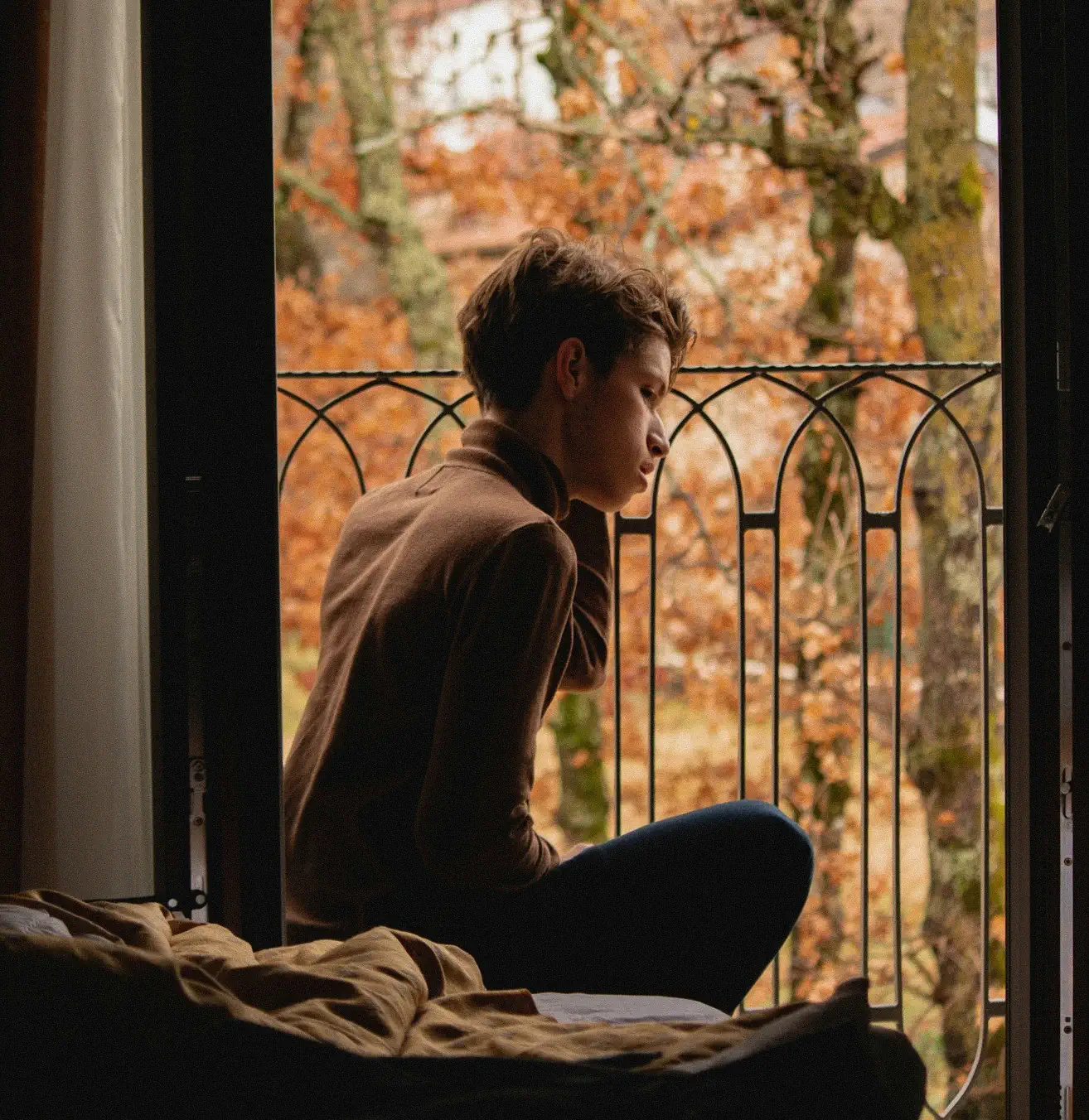 Sad person by open window with autumn trees in background