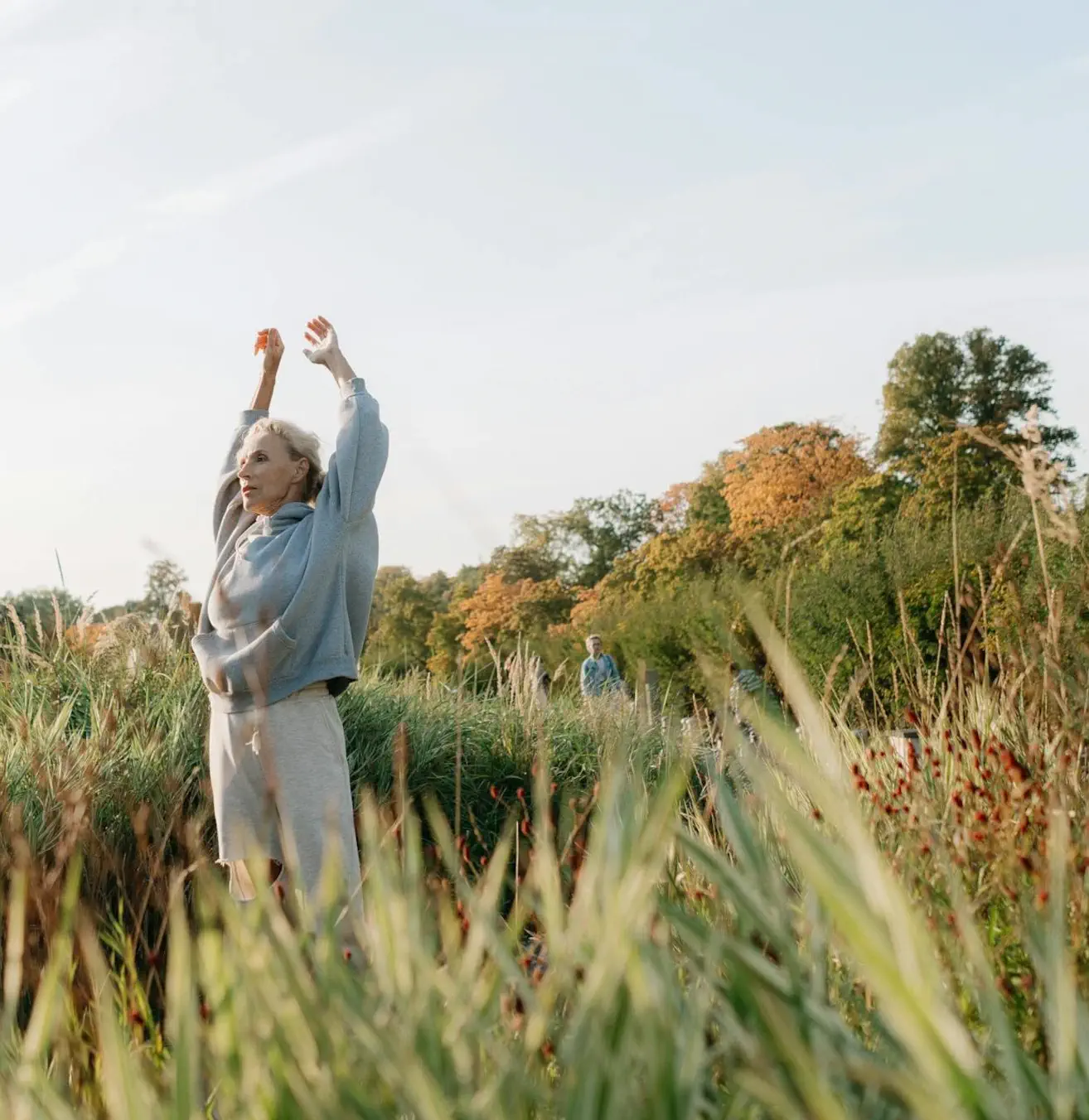Senior woman stretching in a sunny, lush-green park.