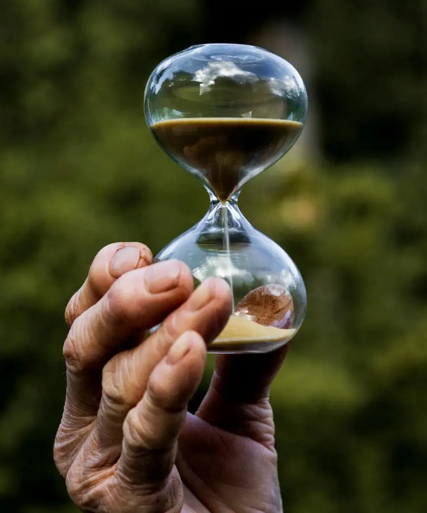 Close up image of hand holding an hour glass with blurred nature background.