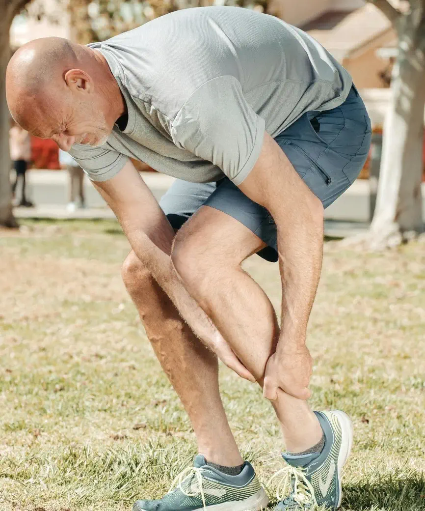 Older man outside holding his hurt calf/ankle.