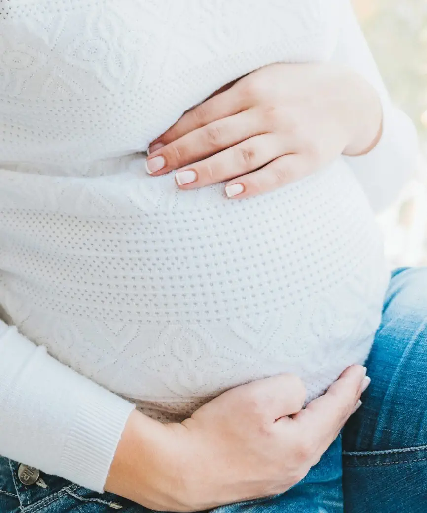 Gros plan des mains d'une femme sur son ventre enceinte sur une chemise blanche